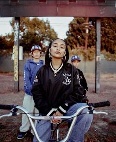 a woman sitting on top of a bike next to two boys standing behind her and holding onto the handle bars