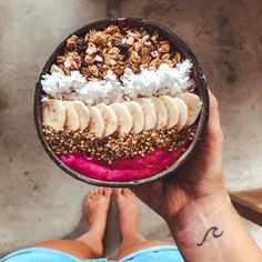 a person holding up a bowl filled with fruit and granola on top of it