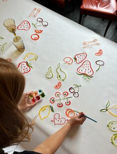 a woman is drawing on a table with fruit and vegetables drawn on it in bright colors