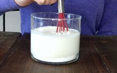 a person whisk milk in a glass on a wooden table