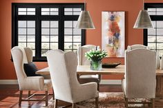 a dining room with orange walls and white chairs around a wooden table surrounded by beige upholstered chairs