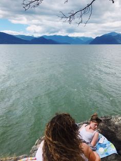 two women are sitting on the rocks by the water looking at something in the distance