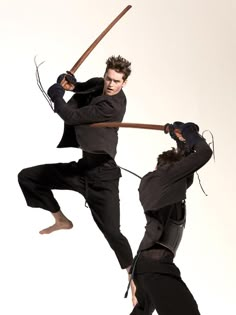 two young men are practicing martial moves with swords