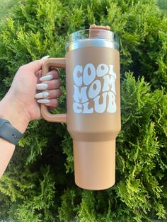 someone holding a coffee cup with the words cool mom club on it in front of some bushes