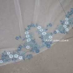 a white and blue floral embroidered lace on a piece of fabric with some light blue flowers