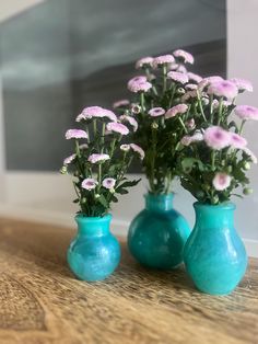 three blue vases with pink and white flowers in them on a wooden table top