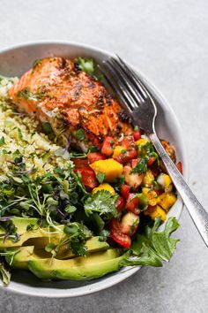 a white plate topped with salmon, rice and veggies next to a fork