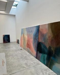 three abstract paintings are on display in an art gallery with white walls and concrete flooring