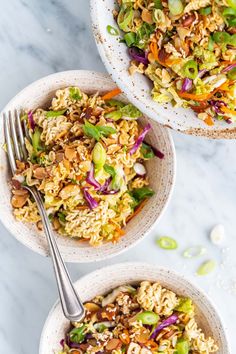 two bowls filled with rice and vegetables on top of a white table next to a fork