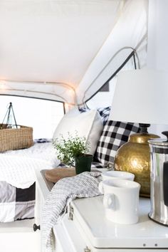 the interior of a camper with pillows, blankets and coffee mugs on it