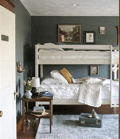 a white bunk bed sitting in a bedroom next to a wooden table and chair on top of a blue rug