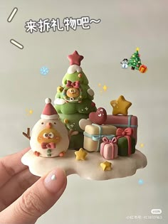 a hand holding up a small christmas tree with presents on it and other decorations around it