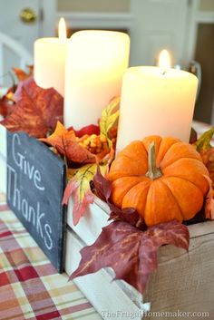 some candles are sitting on a table with fall leaves and pumpkins around it,