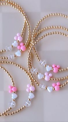 three necklaces with pink and white heart charms on gold beaded chains, one is decorated with hearts