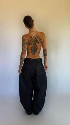 a woman with tattoos on her back standing in front of a white wall and wearing black jeans