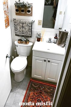 a white toilet sitting next to a sink in a bathroom under a mirror with plants on it