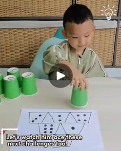 a young boy sitting at a table with green cups and paper cones in front of him