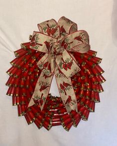 a red and gold christmas wreath on a white background with ribbon hanging from the front