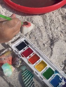 someone is painting shells on the beach with water and paintbrushes in their hands