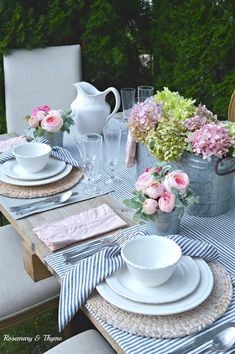 the table is set with plates, cups and vases filled with pink flowers on it