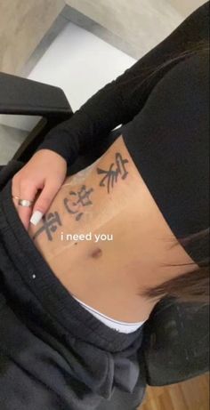 a woman with tattoos on her stomach writing i need you written in chinese characters behind her