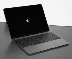 an open laptop computer sitting on top of a gray table next to a white wall