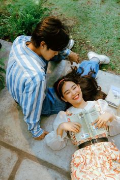 two people laying on the ground and one is reading a book