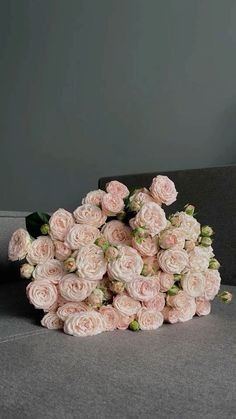 a bouquet of pink roses sitting on top of a gray couch in front of a grey wall