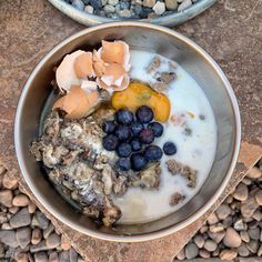 two bowls filled with food sitting on top of a stone floor next to gravel and rocks