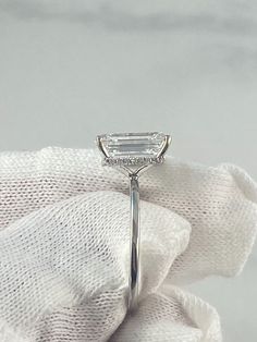 a white gold ring with an emerald cut diamond set in the center, on top of a white cloth