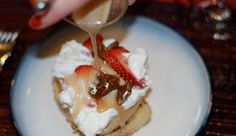 a plate with waffles, whipped cream and strawberries on top is being drizzled with syrup