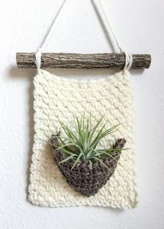 a crocheted planter hanging on a wall with a wooden stick attached to it