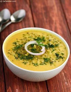 a white bowl filled with soup on top of a wooden table next to spoons