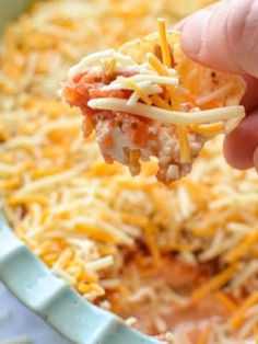 a hand holding up a piece of food with cheese and sauce on it in a casserole dish