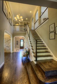 an entryway with stairs and pictures on the wall above it, along with a wooden floor