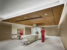 two men in red uniforms standing around a hospital room with a large machine on the floor