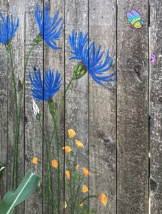 blue flowers painted on the side of a wooden fence with butterflies flying over them and in front of it