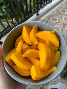 a person holding a bowl full of cut up mangoes