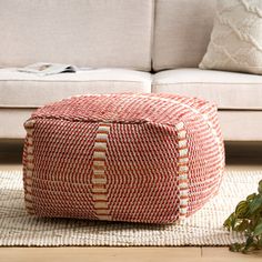 a red and white ottoman sitting on top of a wooden floor next to a couch