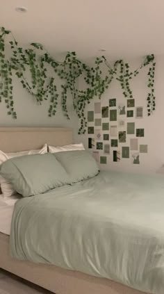 a bed with green sheets and pillows next to a plant on the wall above it