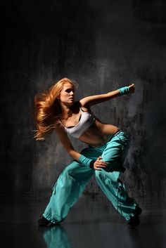 a woman with red hair is dancing in blue pants and white tank top, black background