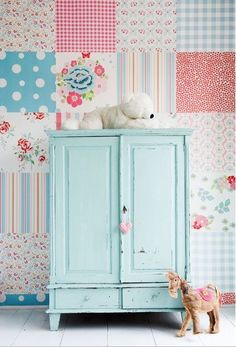 a small toy horse standing next to a blue cabinet with flowers on the wall behind it