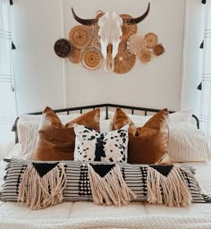 a bed topped with lots of pillows next to a wall mounted cow skull on the wall