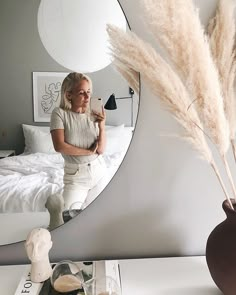 a woman standing in front of a mirror next to a table with a vase on it