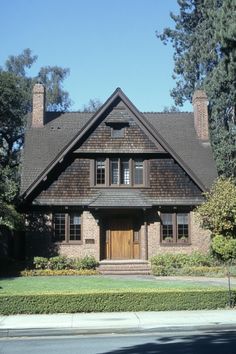 a large brown brick house sitting on the side of a road next to a lush green forest