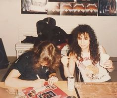 two young women sitting at a table in front of books and papers, one holding a drink