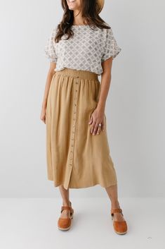 Start your day in style with the 'Greta' Skirt! This midi length, linen-blend skirt is light and airy for spring and summer and features button-down detailing for a fun touch. Pair the 'Greta' with all your favorite tops for Sunday morning or a day at the farmer's market! 30% Linen 70% Rayon Hand Wash Cold Hang to Dry Low Iron if Needed Do Not Dry Clean Fully Lined Model in Ochre Height 5'5" | Wearing Size Small Wearing 'Shalom' Geometric Print Top in Tan & 'Greta' Linen Blend Midi Skirt in Ochr Skirt And Blouse Outfits, Linen Skirt Outfit, Cotton Skirt Outfit, A Line Skirt Outfits, Farmers Market Outfit, Clogs Outfits, Skirt Outfit Fall, Casual Mom Style, Linen Midi Skirt