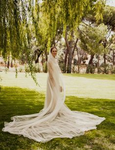 a woman in a wedding dress standing under a tree with her veil draped over her head