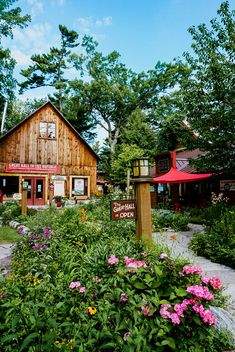 an old wooden building surrounded by flowers and greenery in the foreground is a sign that reads,