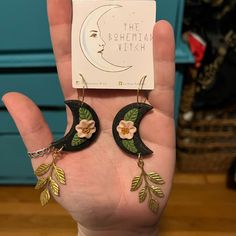 a hand holding a pair of earrings with leaves and flowers on the bottom of it